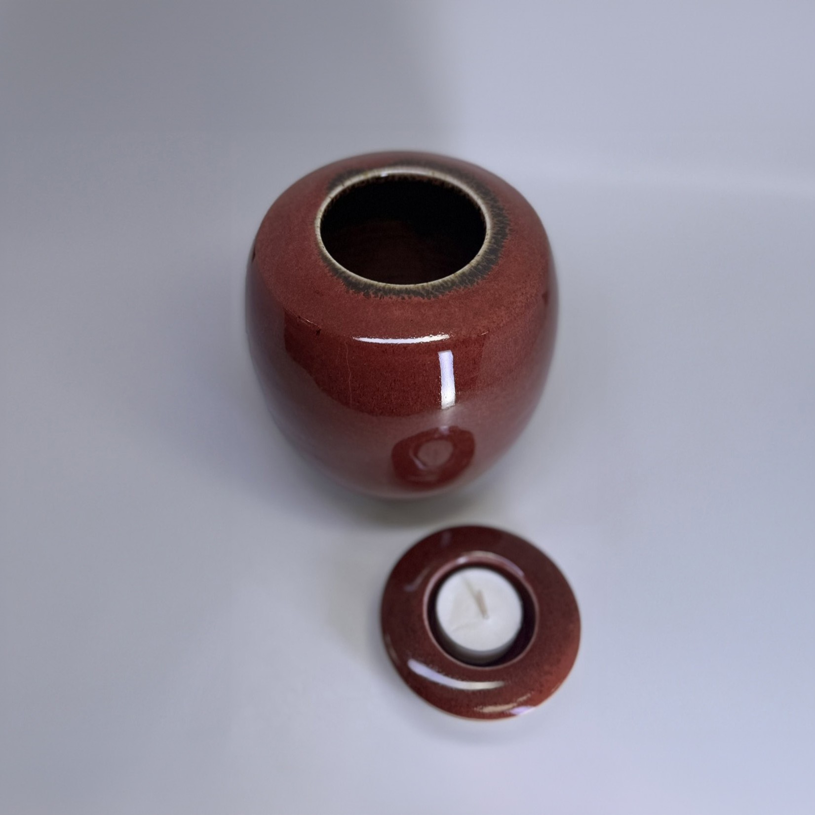 Small ceramic urn with removable candle holder lid shown separately in ember red glaze