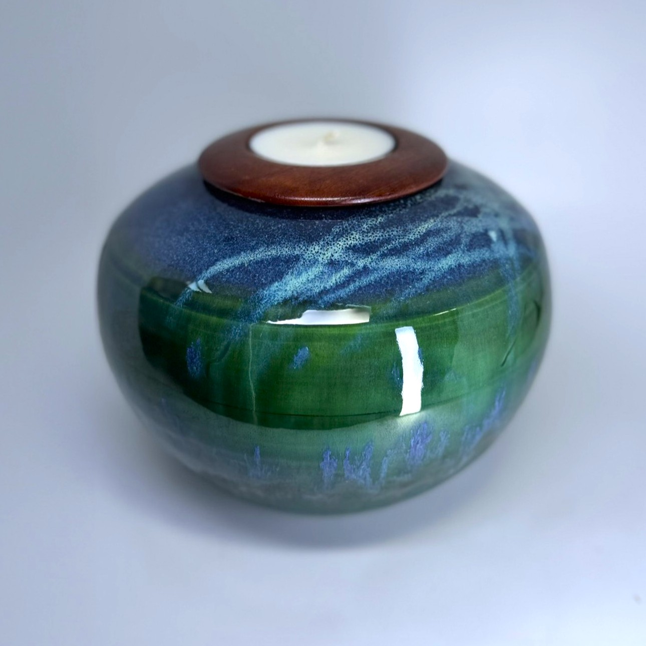 Ceramic cremation vessel with nature-inspired green and blue layered glaze and tealight holder