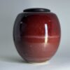 Handmade ceramic urn in deep red with black lid showing glossy flame-inspired glaze