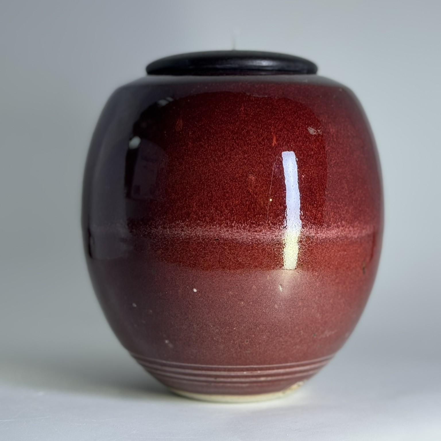 Handmade ceramic urn in deep red with black lid showing glossy flame-inspired glaze